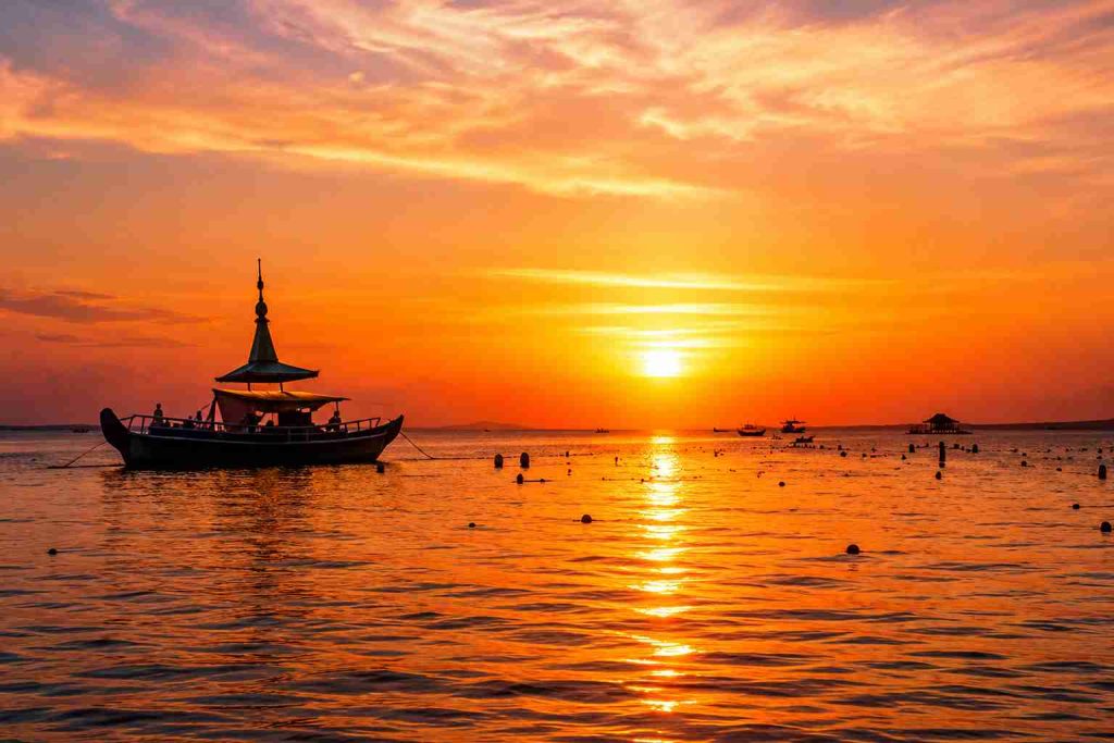 Traditional boat sailing at sunset in Bunaken, North Sulawesi, Indonesia, with golden reflections across calm tropical waters and a vibrant evening sky | Komera.net